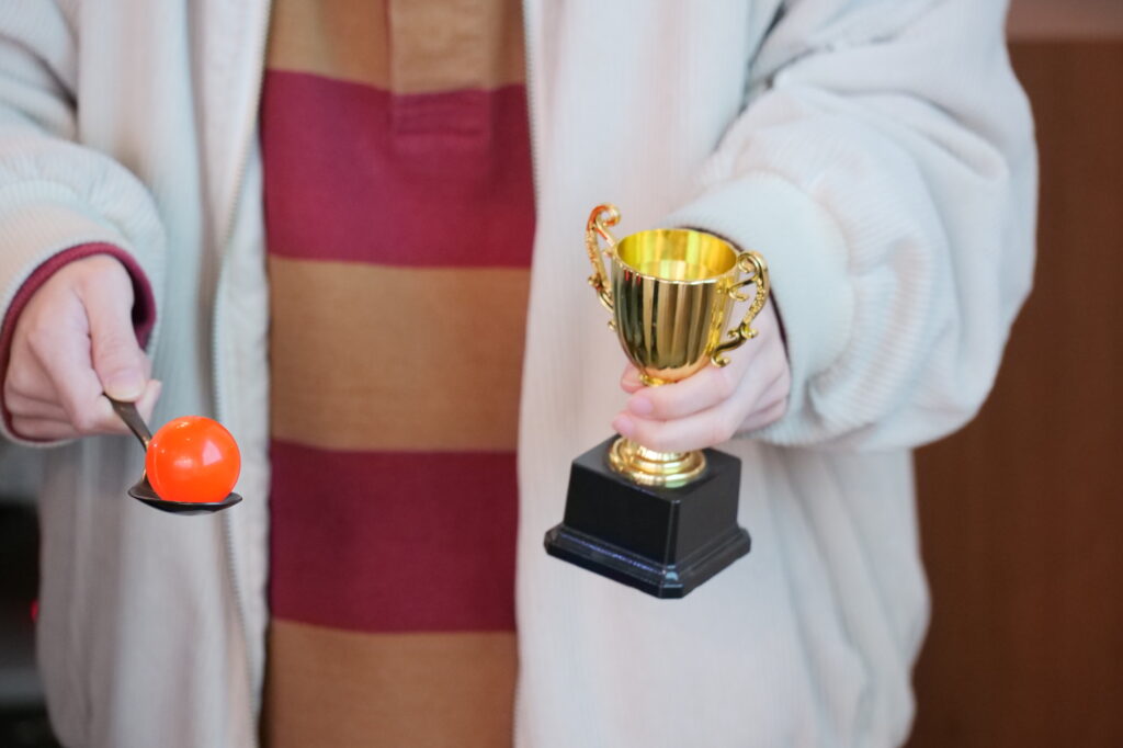 ピンポン玉を乗せたスプーンとトロフィーを手にするメンバー